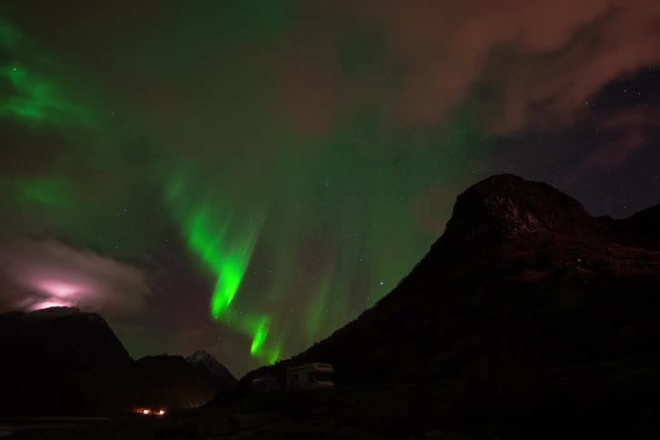 A stunning time-lapse captures the vibrant green Aurora Borealis dancing across the starry night sky above a mountainous landscape