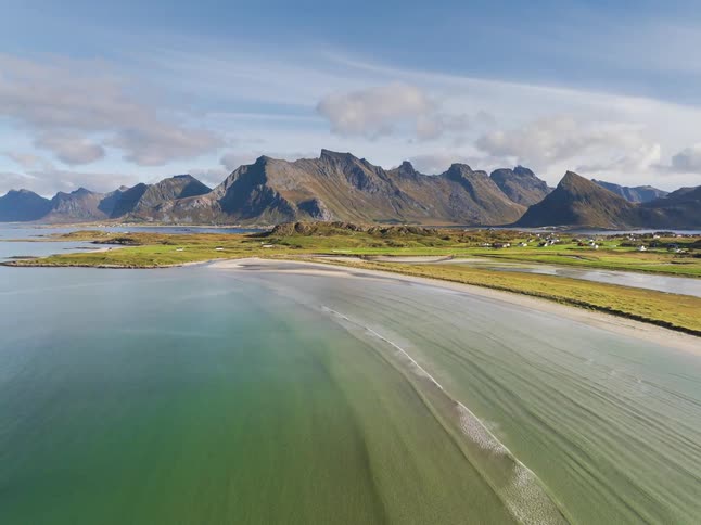 A breathtaking aerial shot rises over a tranquil bay, revealing a stunning sandy beach and a majestic mountain range