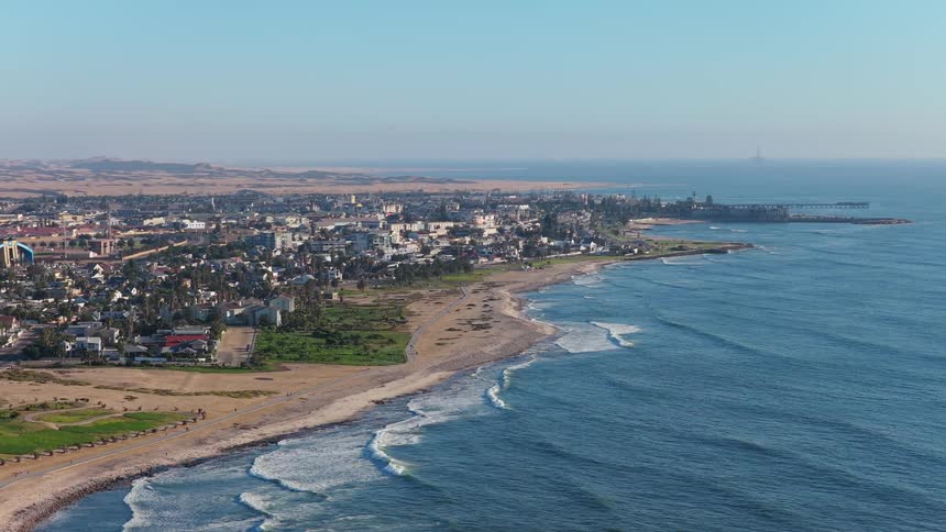 An expansive aerial view of the coastal city Swakopmund in Namibia, where the vast desert meets the rolling waves of the Atlantic Ocean on a clear day