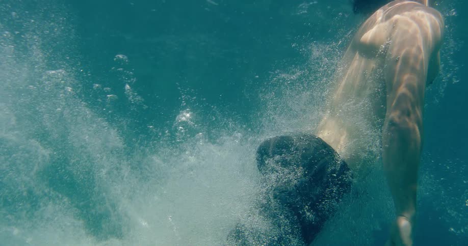 Underwater slow-motion view of a man in swim trunks diving headfirst into the clear blue ocean