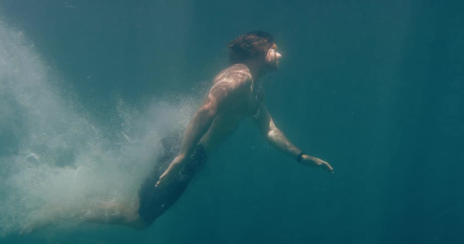 Slow motion underwater shot of a man diving into the turquoise sea and gliding peacefully