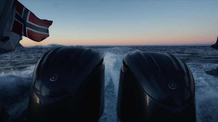 Slow motion shot from the back of a speeding boat shows two powerful outboard motors creating a wake in the Norwegian sea at sunset