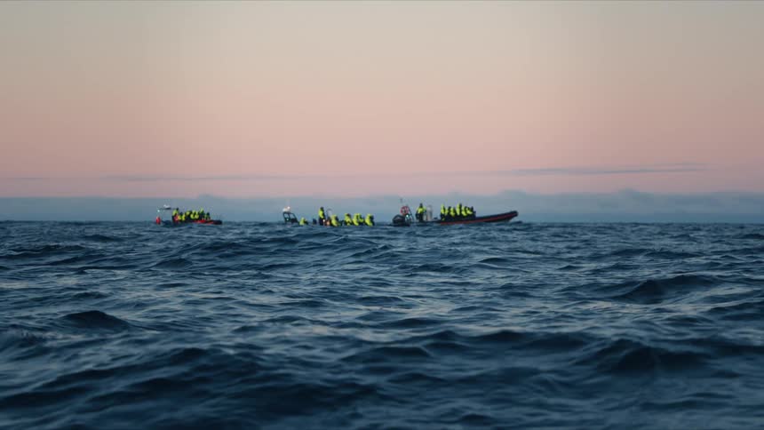 Rescue team boats and swimmers in yellow life jackets float on the choppy ocean during a twilight training exercise