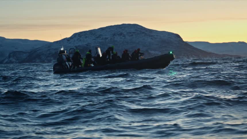 Adventurous travelers on a rigid inflatable boat explore the arctic ocean at dusk, surrounded by snow-capped mountains