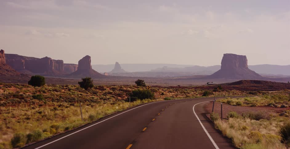 Aerial drone footage smoothly follows a winding road through the vast desert landscape of Monument Valley, Arizona