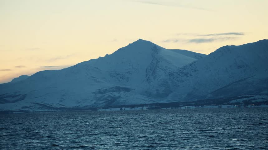 A serene view of snow-capped mountains across a dark, rippling fjord at twilight in a Nordic landscape
