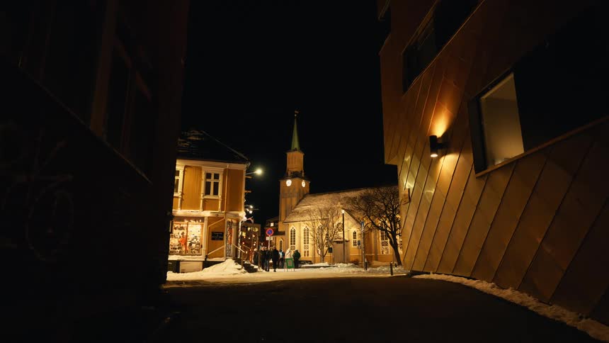 Townsfolk gather outside a beautifully lit church on a cold, snowy night in a quaint European village