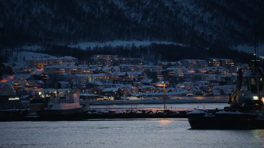 A picturesque winter evening in a snowy Norwegian harbor town, with cozy lights illuminating the houses against a dark mountain backdrop