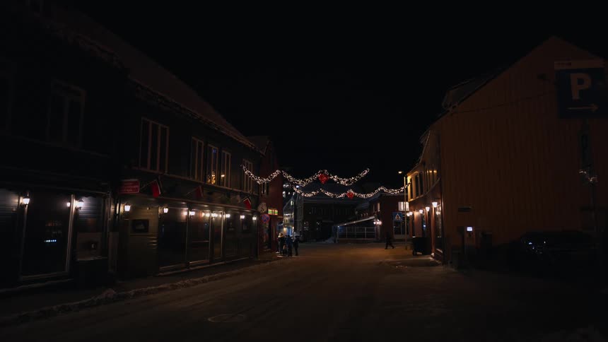 A peaceful, snowy town street is beautifully decorated with glowing Christmas lights on a quiet winter night