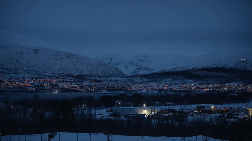 A serene Nordic town glows with warm lights, nestled in a vast, snowy mountain valley during the deep blue twilight of a winter night