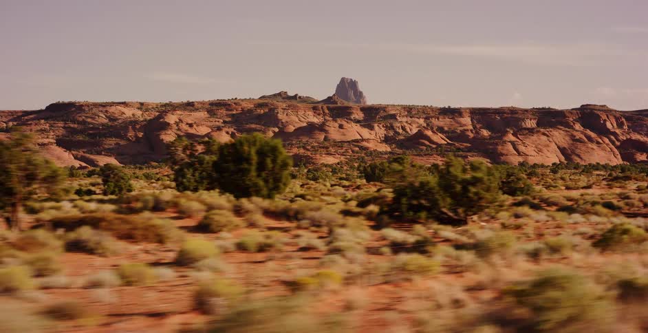 Scenic driving shot past the arid desert landscape and red rock buttes of the American Southwest