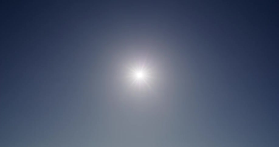 A static shot of the bright sun shining in a clear, cloudless blue sky