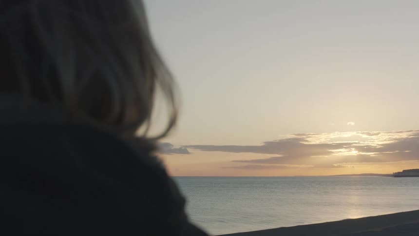 A woman with blonde hair gazes peacefully at the serene sunrise over the ocean