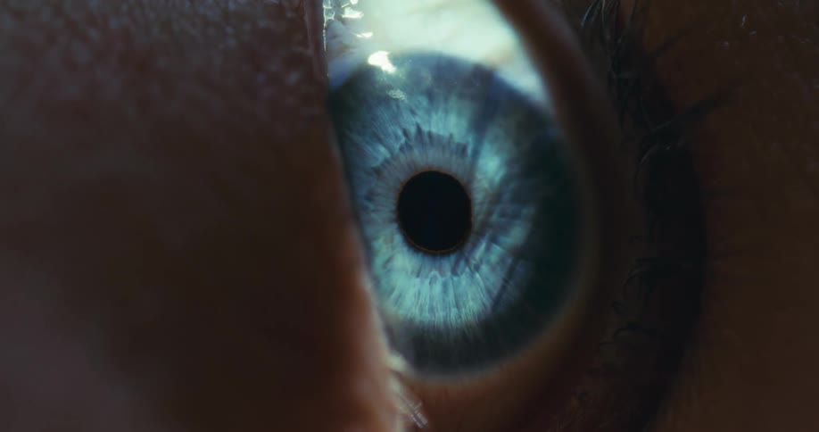 An intense macro shot captures the intricate details of a blue human eye as it slowly gazes forward