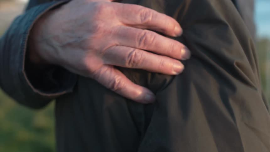 In slow motion, an older person's hand gently rests on a shoulder in a comforting and supportive gesture outdoors