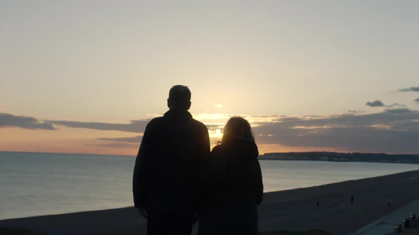A silhouetted couple stands together and enjoys the view of a beautiful sunset over the ocean beach