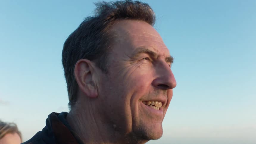 A content older man smiles warmly while looking out over the ocean as the sun sets