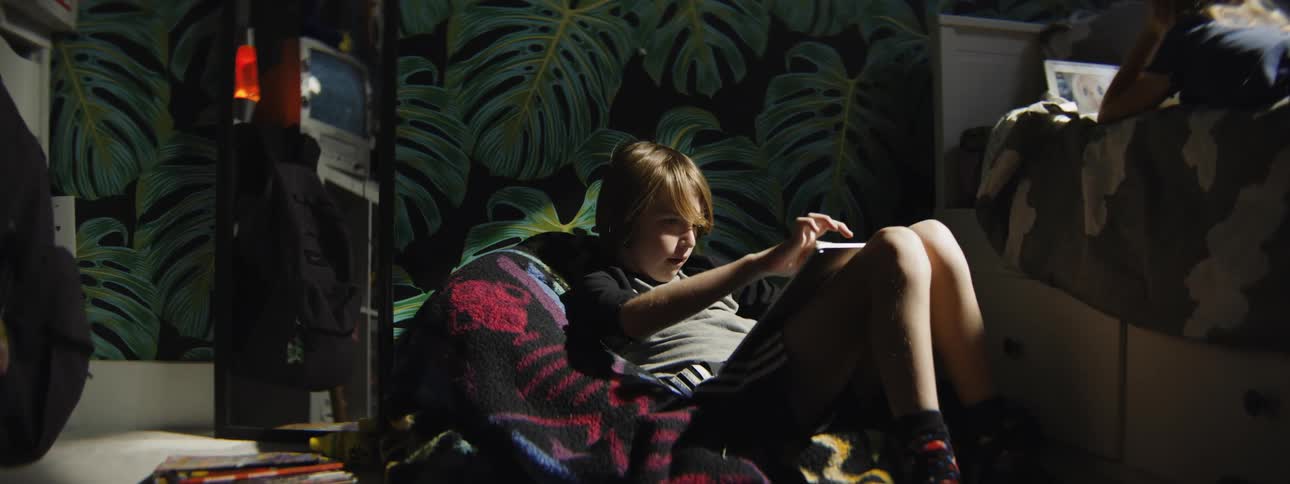 Slow zoom in on a young boy smiling and excitedly playing a video game on a digital tablet in his bedroom