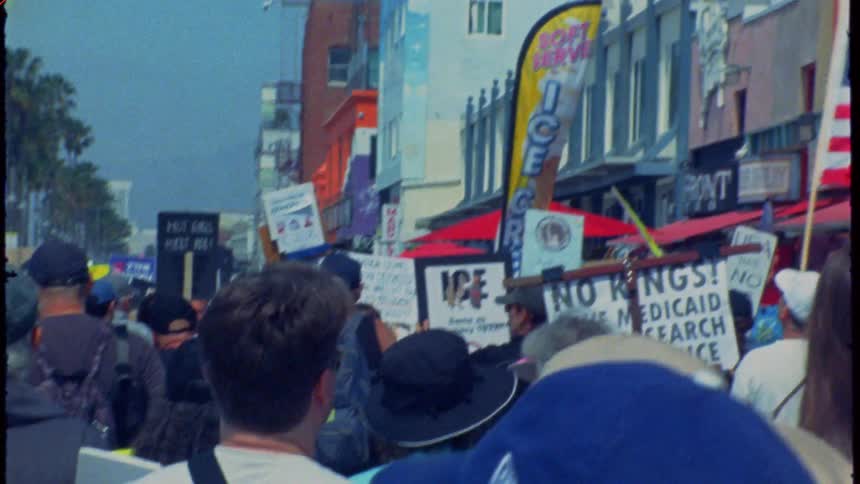 Retro-style film footage captures a crowd of protestors marching with signs down a palm tree-lined city street