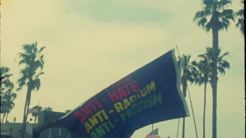 Vintage-style, slow-motion footage of anti-Trump and 'Resist' protest flags waving beneath California palm trees