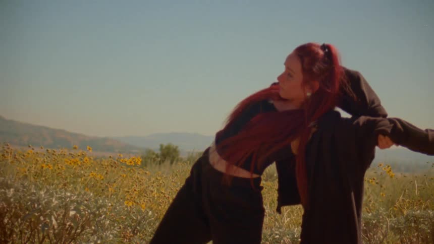 An expressive dancer with vibrant red hair performs a slow-motion routine in a sun-drenched field of wildflowers