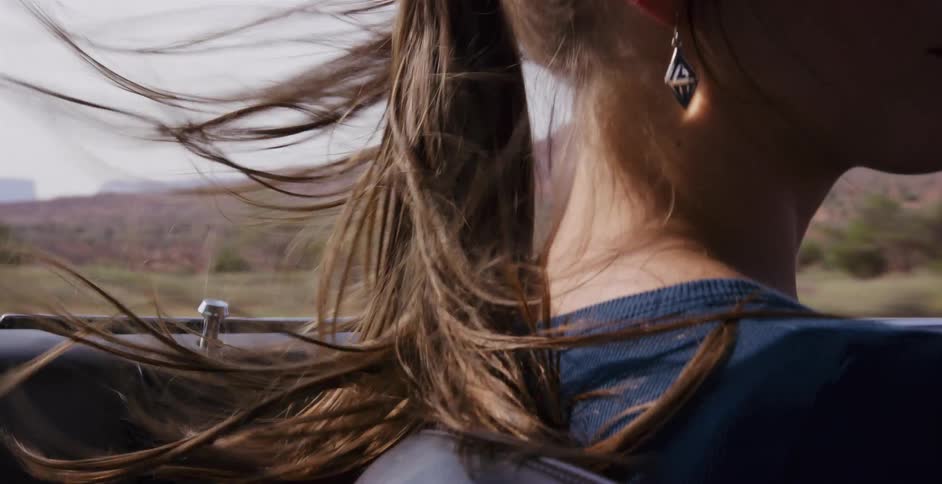 The wind blows through a woman's brown ponytail as she enjoys a carefree ride in a convertible through a desert landscape
