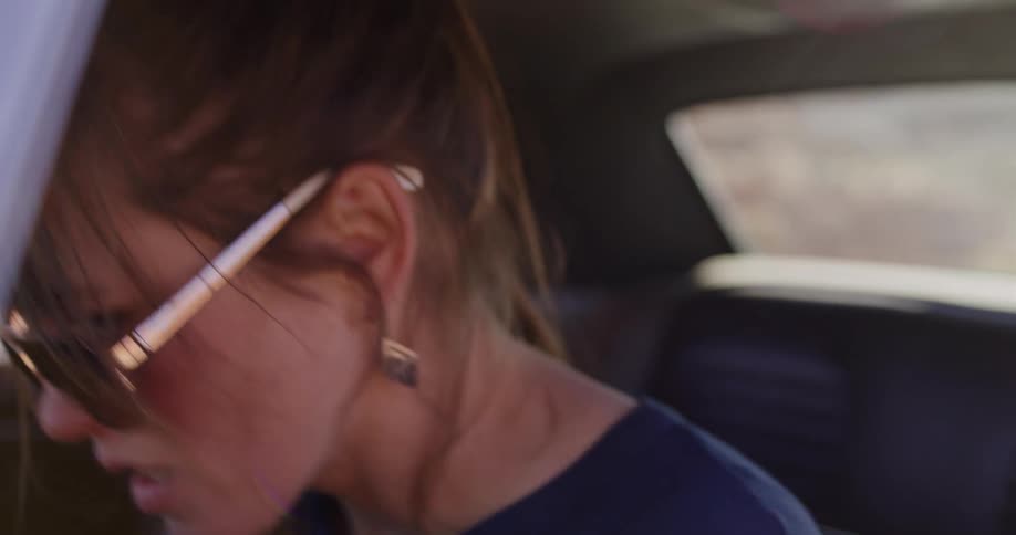 A happy woman in sunglasses enjoys a car ride in slow motion, smiling and tossing her hair around