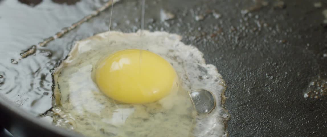 Egg white and yolk dropping onto hot sizzling pan and cooking