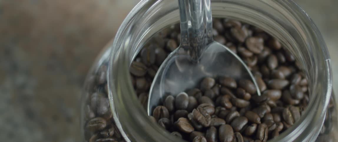 Someone scoops out coffee beans from a jar