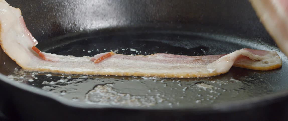 Bacon being set in a frying pan