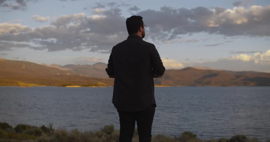 A man takes a photo of a beautiful mountain lake at sunset before taking in the serene view