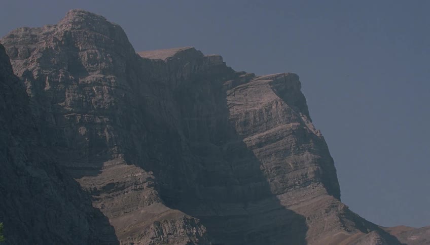 A static shot of a majestic, rocky mountain peak against a clear blue sky on a sunny day