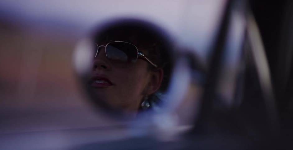 Slow motion reflection of a stylish woman in sunglasses smiling while driving in a car at dusk