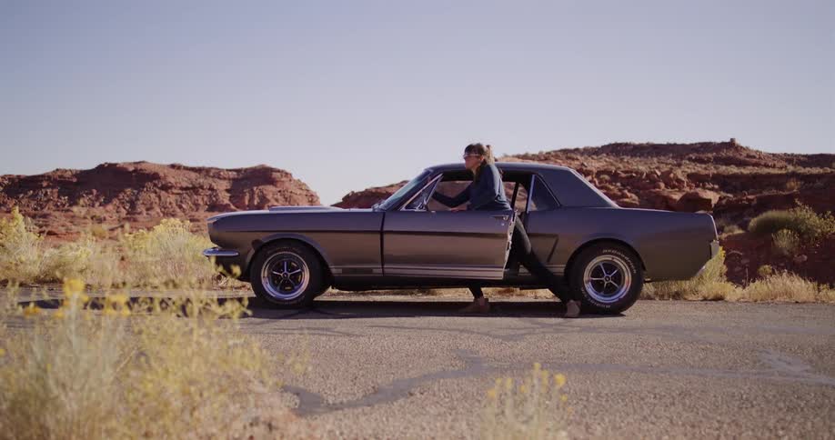 A woman stranded with her broken-down classic Ford Mustang on a remote desert road tries to push it by herself