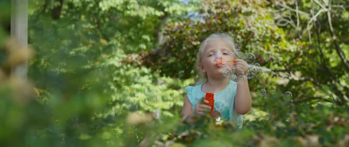 A young girl blows bubbles with trees all around