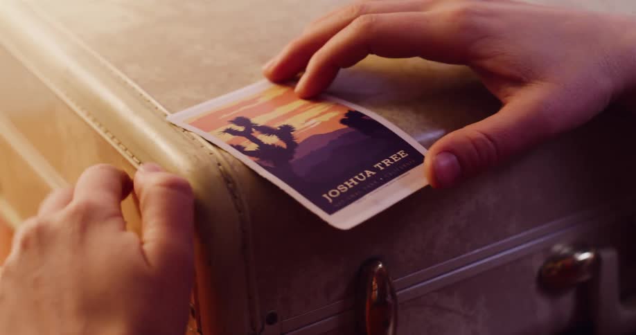 A close-up shot of hands carefully placing a Joshua Tree National Park travel sticker onto a vintage suitcase