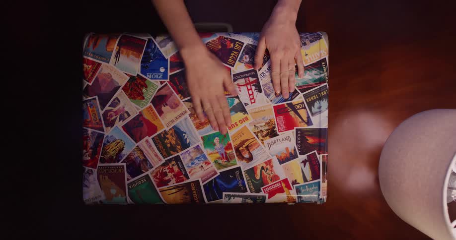Overhead shot of a person's hands caressing a suitcase covered in travel stickers and postcards