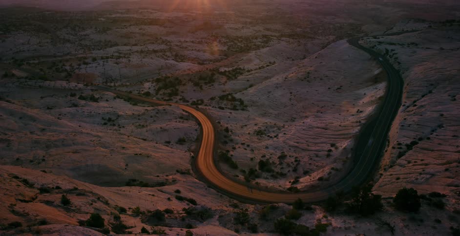 Time-lapse of cars and trucks driving along a scenic winding road through a rocky desert canyon during a vibrant sunset