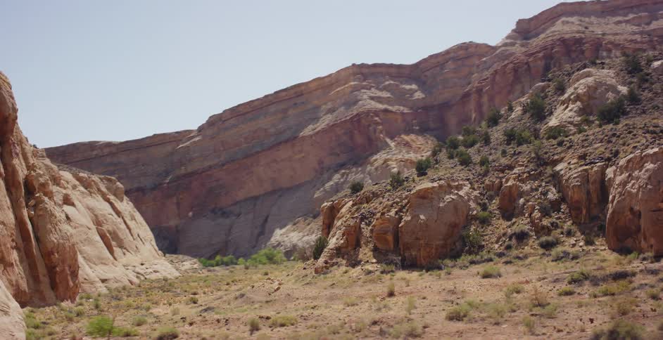 A slow, smooth pan reveals the vast, sun-drenched landscape of a desert canyon with its stunning layered rock formations
