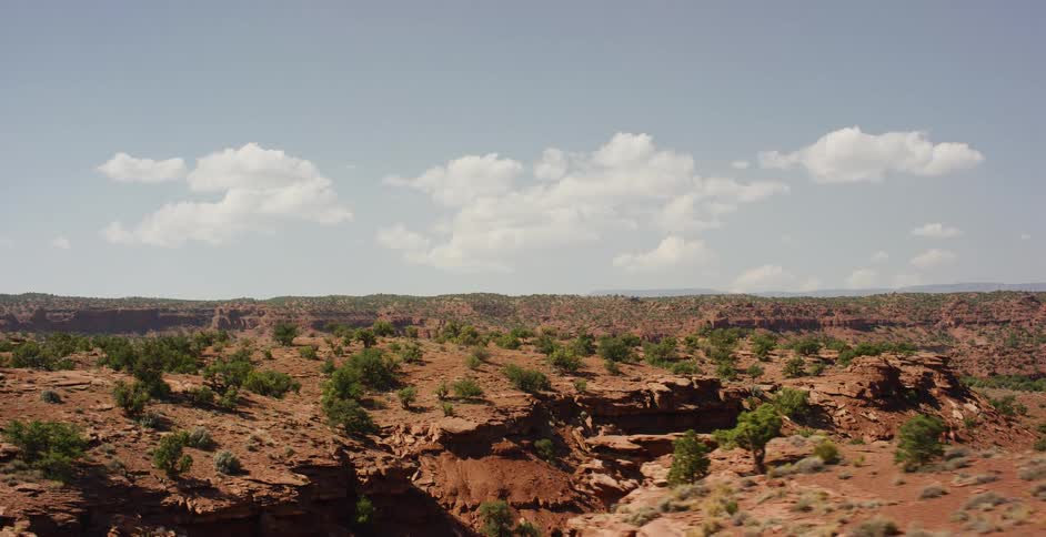 A sweeping view of a vast red rock desert landscape under a partly cloudy blue sky