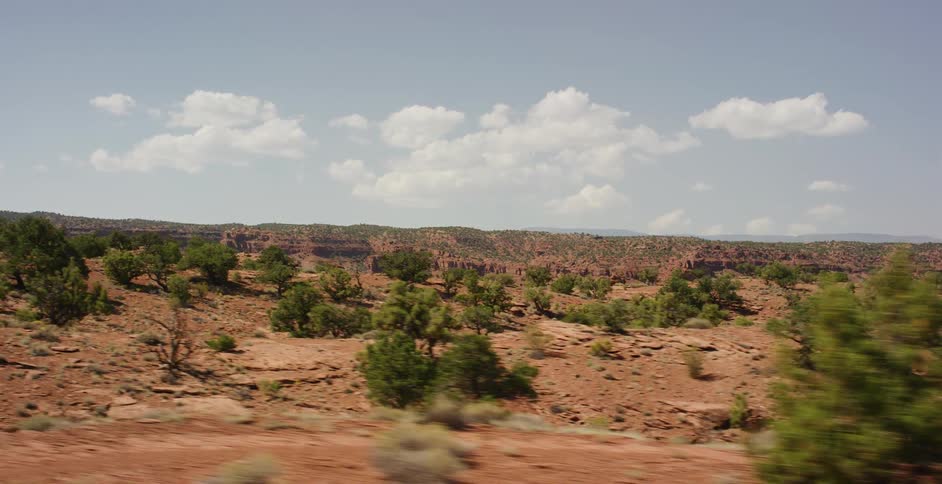 A tracking shot captures the vast red rock desert landscape of the American Southwest on a sunny day with scattered clouds