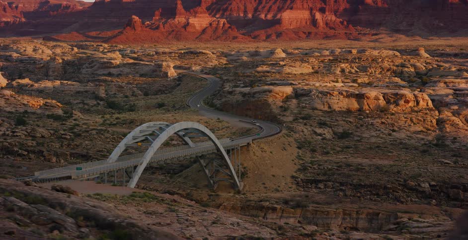 A smooth reveal shot unveils a highway bridge spanning a vast desert canyon with red rock formations at sunrise