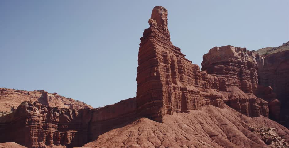 A cinematic aerial shot slowly orbits a majestic red rock spire in a vast desert canyon