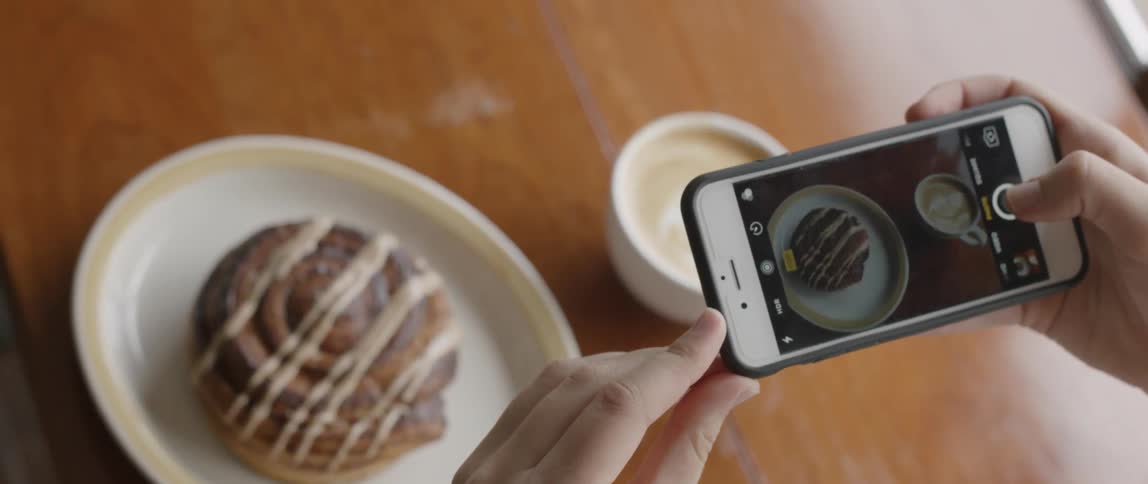 A person photographs a cinnamon roll with a phone