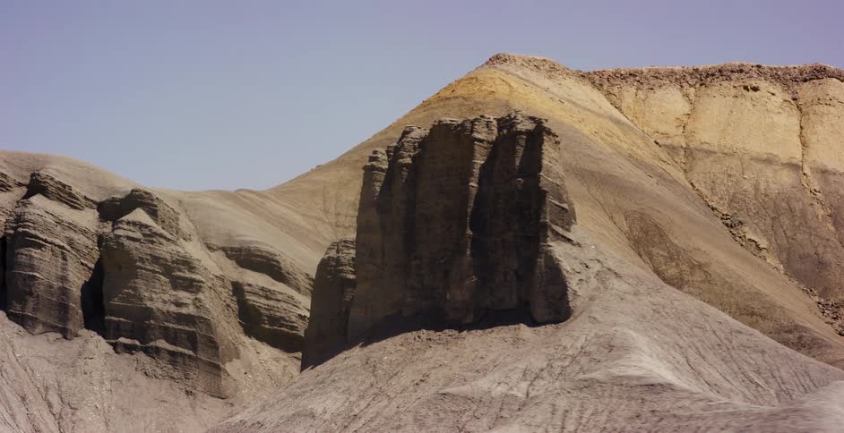 A slow tracking shot pushes in on the majestic, layered rock formations of a vast and arid desert landscape
