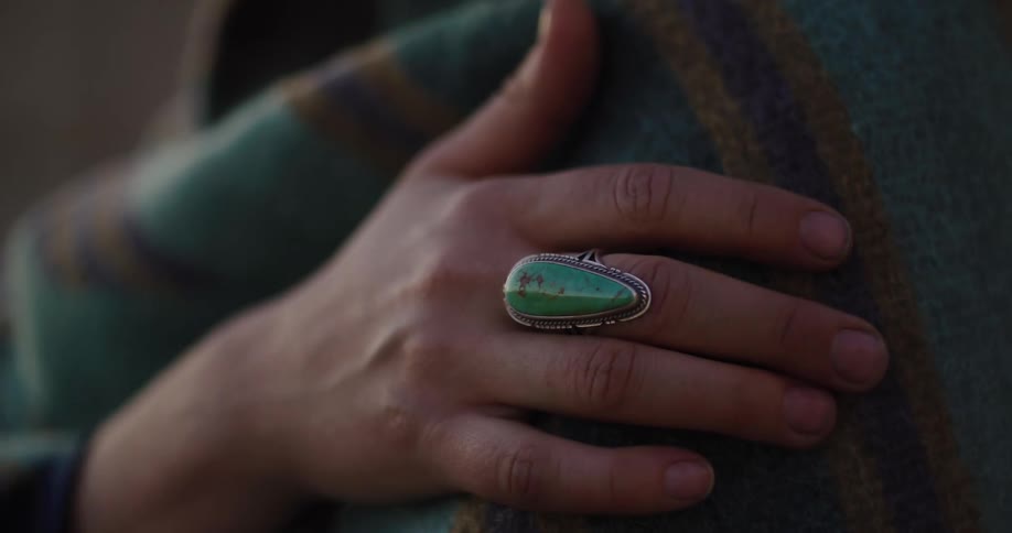 A close-up view of a hand adorned with a large silver and turquoise ring, resting gently on a cozy striped blanket