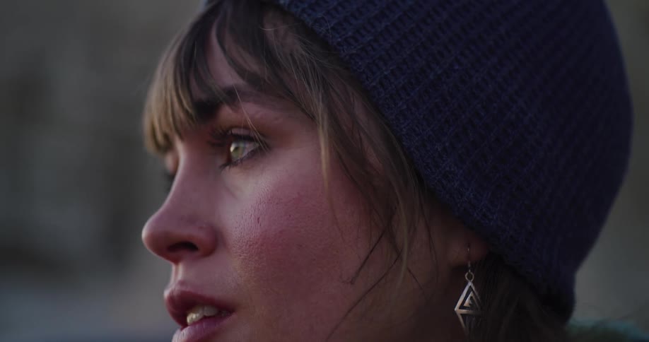 A serene woman with a turquoise ring and a beanie smiles gently while looking into the distance at dusk