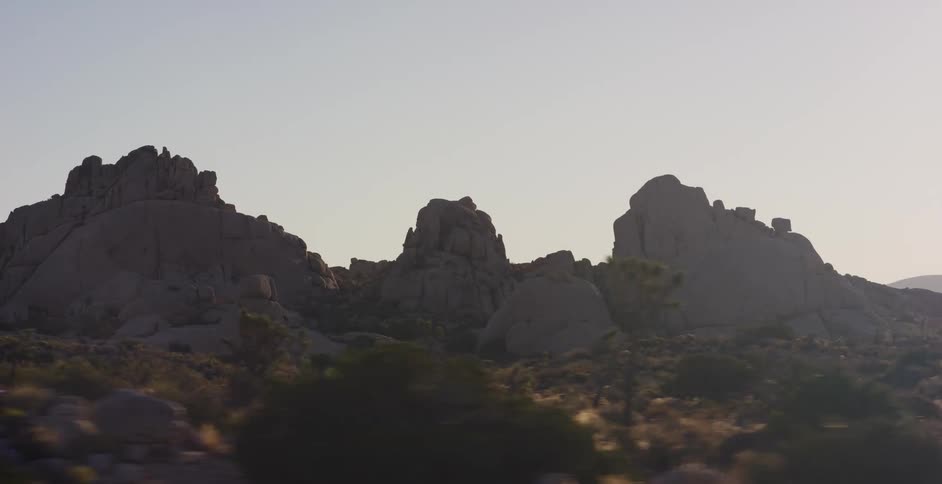 A scenic driving shot reveals the unique rock formations and flora of Joshua Tree National Park at golden hour