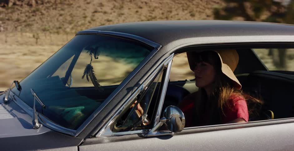 Bohemian-style woman wearing a large sun hat drives a vintage car through the sunny desert