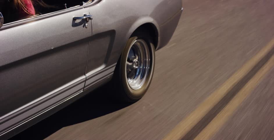 Tight shot of a classic silver Ford Mustang's wheel in motion on a sunny road